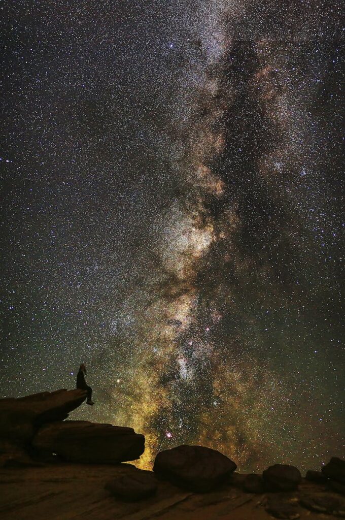 Man in Black Jacket Standing on Rock Formation Under Starry Night