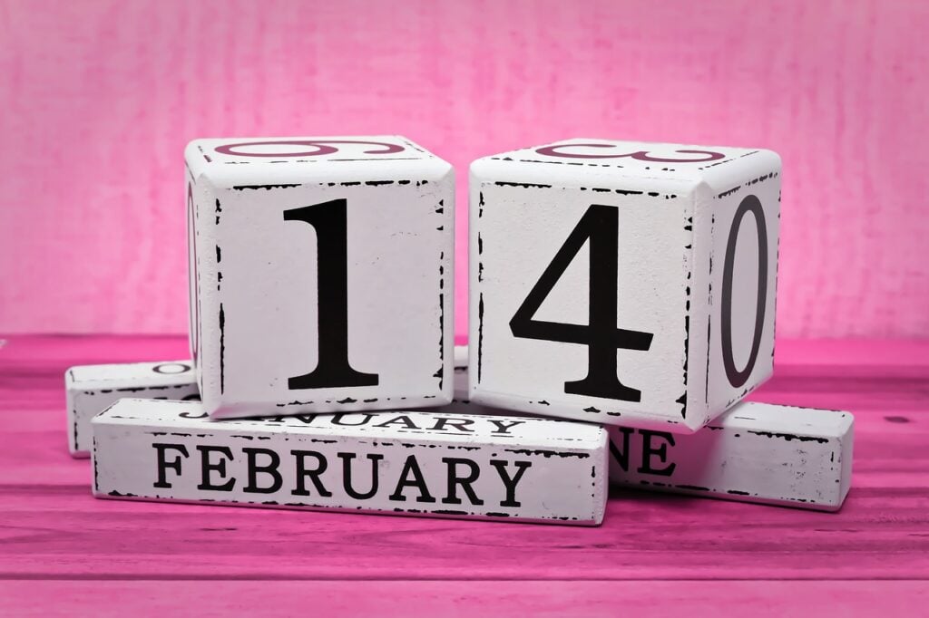 White blocks with February 14 written on them on a pink background for the calendar day of Valentines day