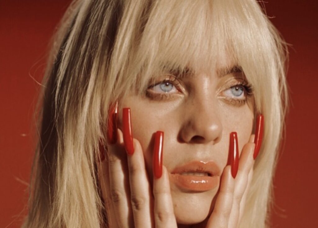 Billie Eilish closeup of her face with her hands on it showing long red nails as accessory for Halloween costume idea. Photo credit: @billieeilish on Instagram via Slowestuff.com