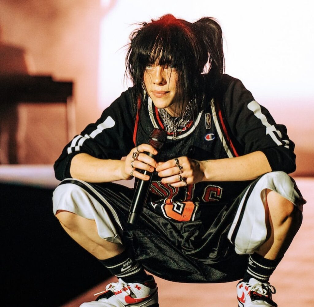 Billie Eilish with red and black hair, dressed in layered streetwear. Iconic Halloween costume inspiration. Photo credit: @billieeilish on Instagram via Slowestuff.com