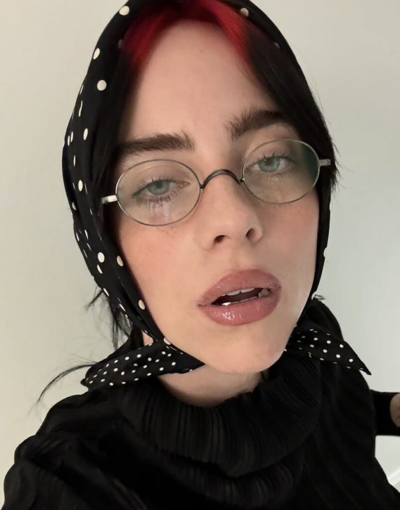 Billie Eilish wearing a polka dot scarf and fashion glasses, a playful take on her Halloween style. Photo credit: @billieeilish on Instagram via Slowestuff.com