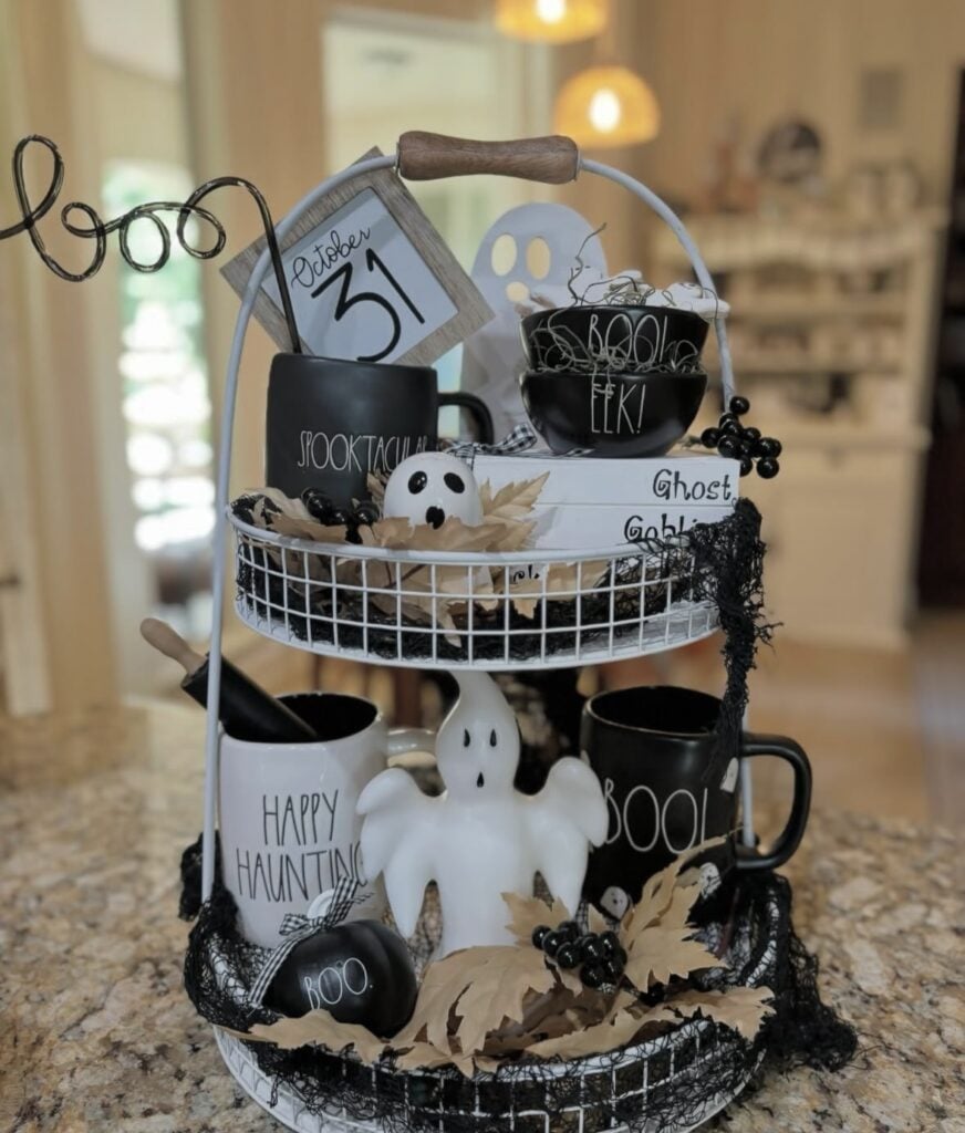 Black and white ghost tiered tray styled with candy corn felt garland, vintage Halloween signs, and a mix of cute ghost figurines for the perfect spooky aesthetic. Credit: lilbitof_berti.