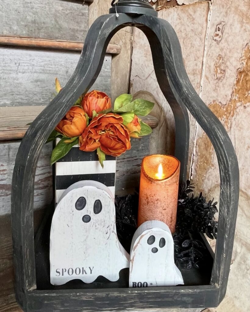 Farmhouse Halloween tray featuring wooden ghost figures, candle and fall flowers styled for an outdoor or entryway space. Credit: mchomeandco.