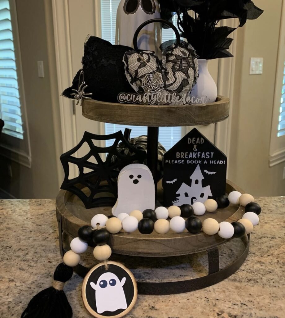 Ghost and haunted house tiered tray loaded with spider web cut out, beaded garland, and a black bouquet—classic Halloween fun! Credit: craftylittledecor.
