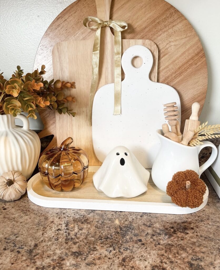 Neutral tiered tray with a ghost mug, soft beige pumpkins, and wooden bead garland for a calm, earthy Halloween vibe—love the natural colors. Credit: raysa_c.g.