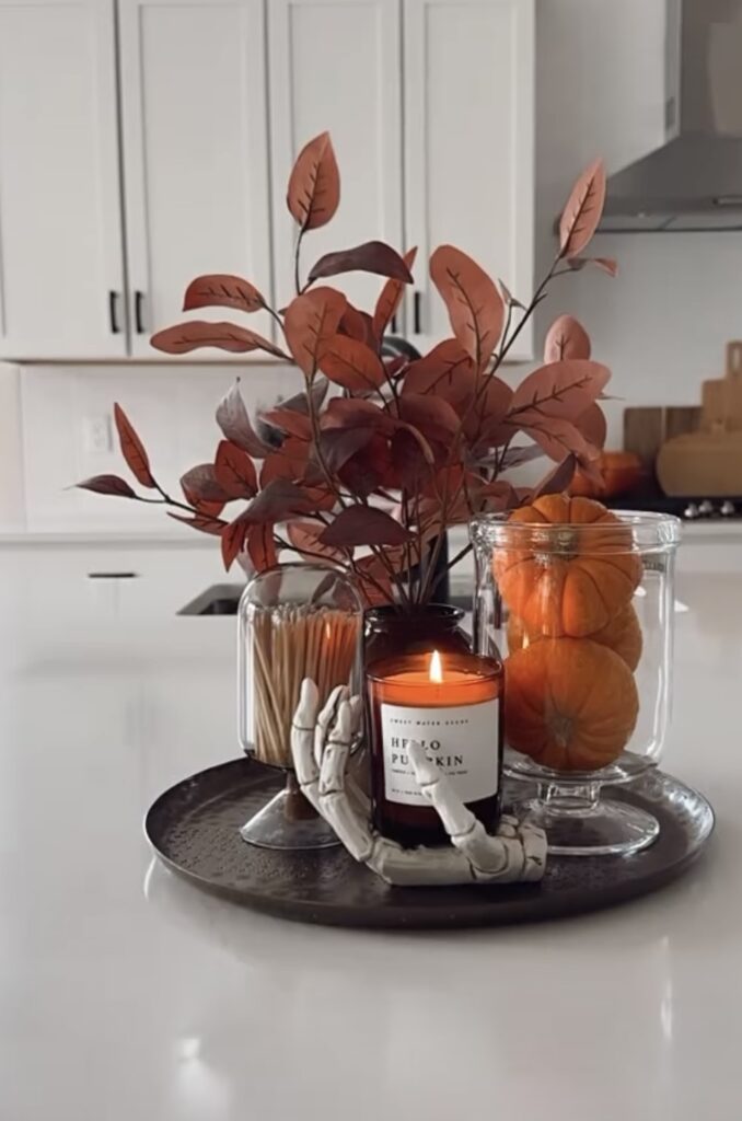 Elegant and simple Halloween tray styled with skeleton hand, fall foliage, mini pumpkins and candle. See more skeleton tray decor ideas at www.slowestuff.com.