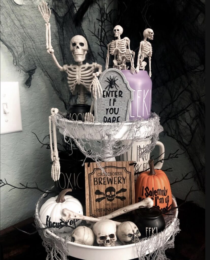 Halloween tiered tray styled with skeletons, mini skulls, bone-shaped props, and festive mugs. See more skeleton tray decor ideas at www.slowestuff.com.