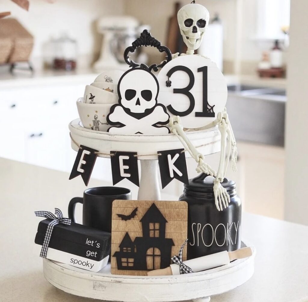 Black and white skulls and skeletons arranged on a tiered tray for Halloween, featuring small pumpkins, spiderwebs, and fun Halloween signs. More at www.slowestuff.com.