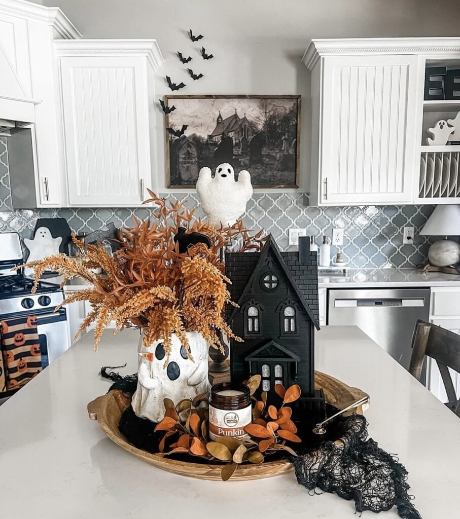 Spooky cute tiered tray decorated with mini ghost figurines, pastel pumpkins, and Halloween mugs—so cozy and haunted! Credit: 12timbers.