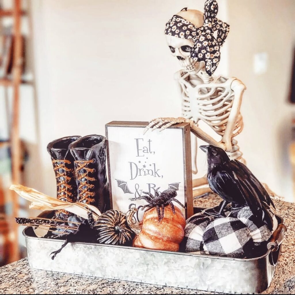 Skeleton with bandana on its head, with raven, black and white checkered decor, pumpkin and raven with sign that says eat drink and be scary arranged on a tin tray for Halloween. More at www.slowestuff.com.