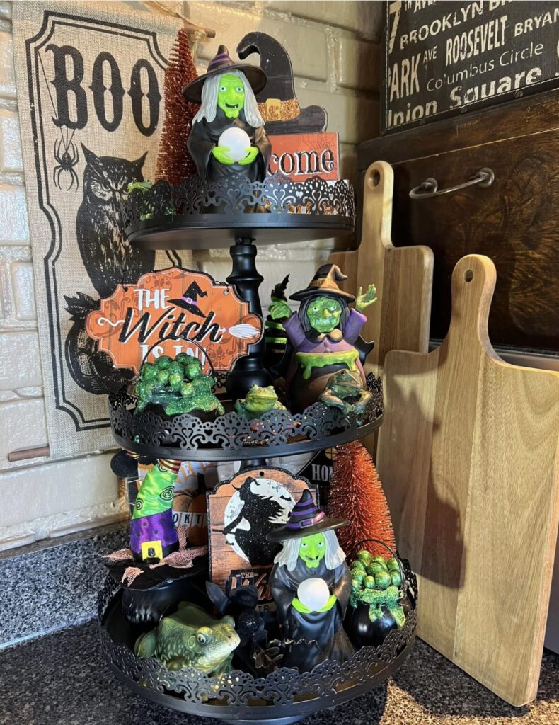 Ornate black Halloween tiered tray with green-skinned witches, witch hats, and a “The Witch Is In” sign. Credit: Bonnie Overman, www.slowestuff.com