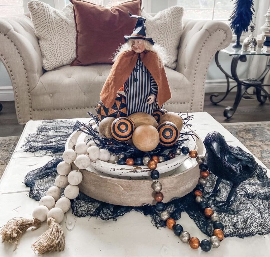 Witch tiered tray centerpiece with witch figurine, raven, wooden beads, twigs, and round ornaments for Halloween. Credit: houseonlouisemeadow, www.slowestuff.com