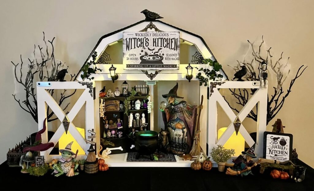 Witch’s kitchen Halloween decor featuring a barn-shaped tray, black cauldrons, candles, pumpkins, and witch hat props. Credit: Brittany Taft, www.slowestuff.com