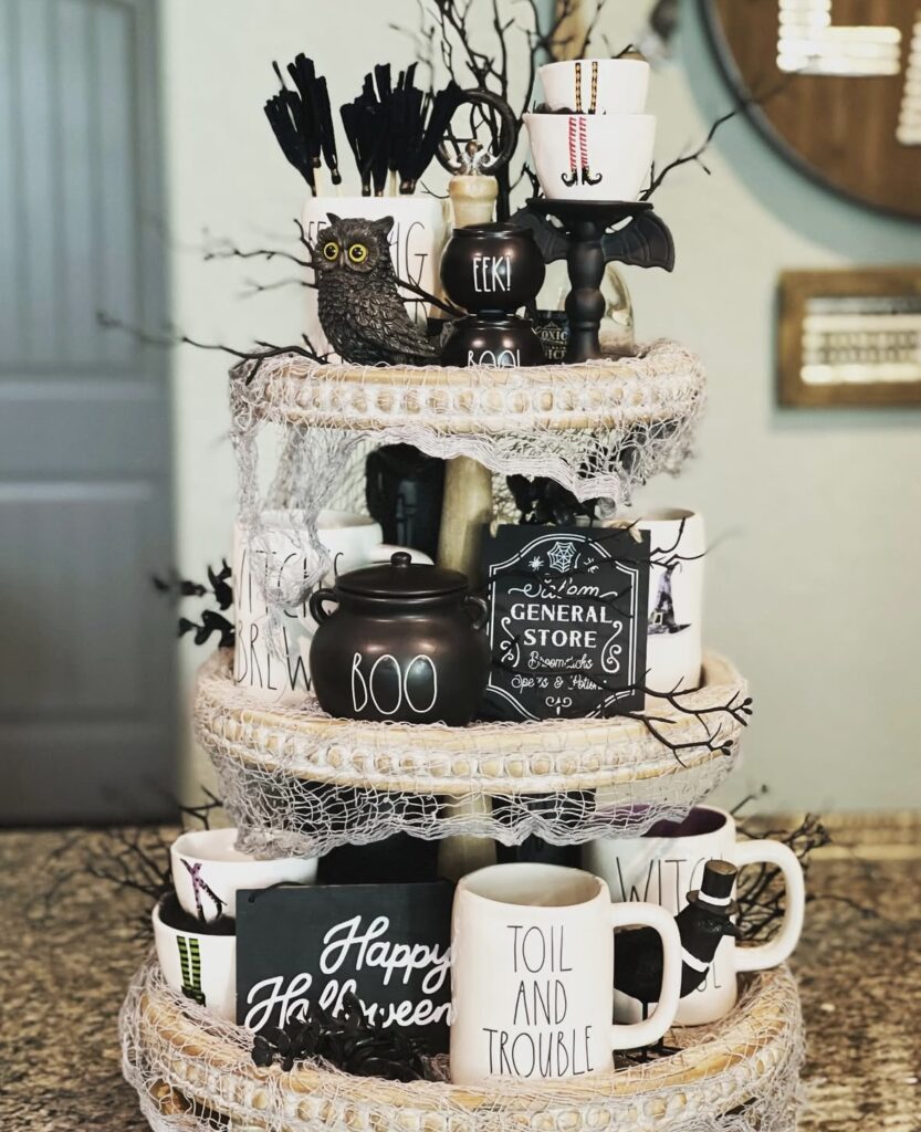 Three-level witchy tiered tray for Halloween with white base, netting, twigs, and stacked witch decor. Credit: designed_comfort_4_5, www.slowestuff.com