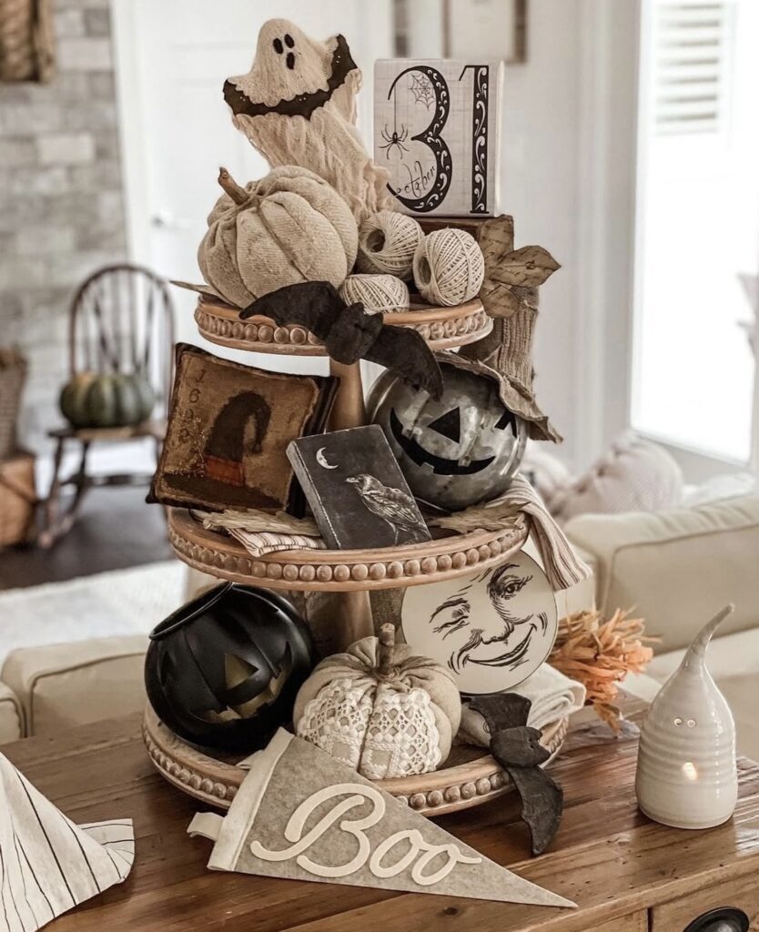 Ghost tiered tray with rich textures: black pumpkins, neutral decor, ghost figurines, and layered beads for major Halloween inspo. Credit: velveteenandgrace.