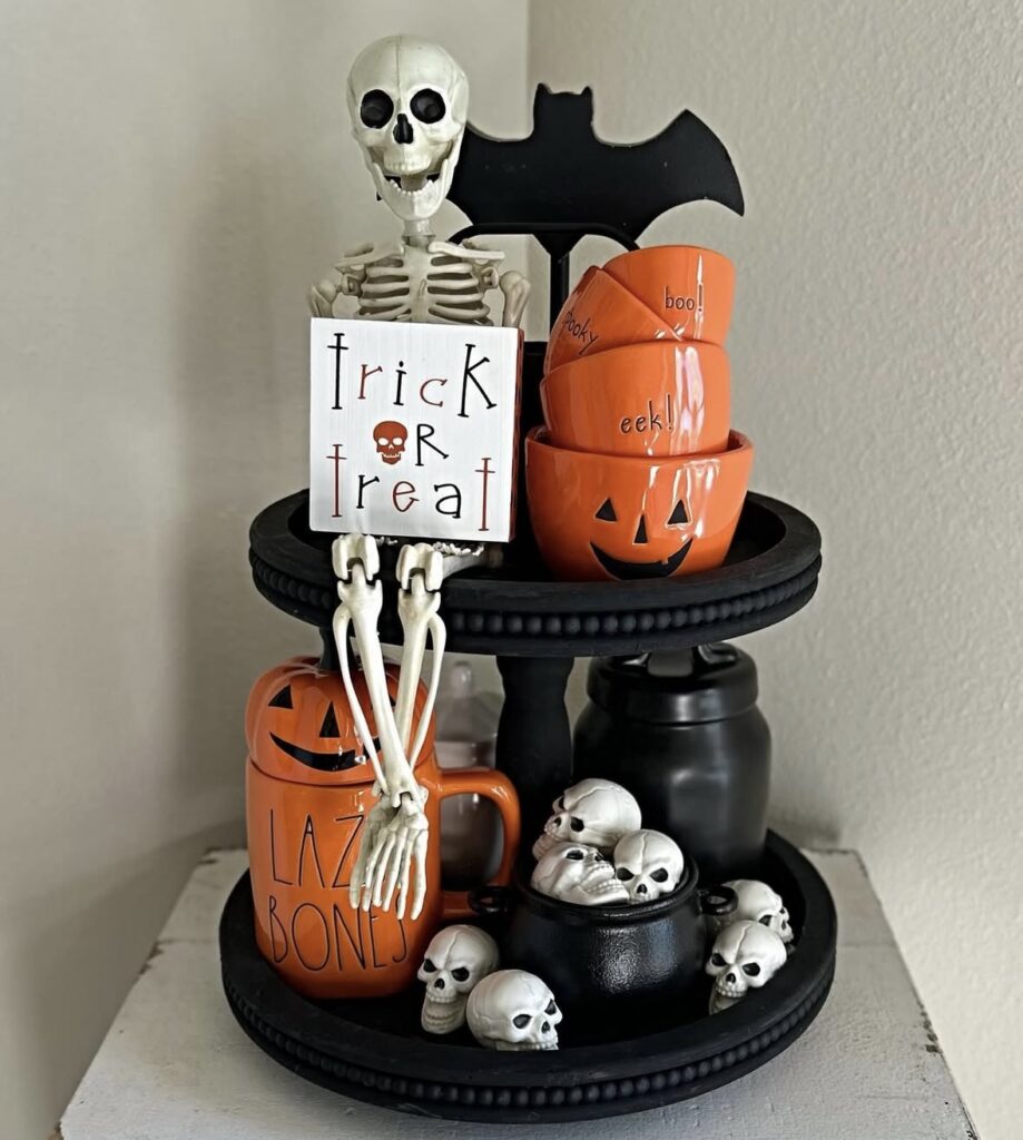 Skeleton-themed tiered tray decorated with tombstone signs, skulls, bone details, and spooky Halloween decor. Get skeleton tray ideas at www.slowestuff.com.