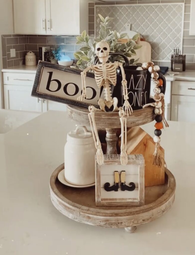 Skeleton tiered tray decorated for Halloween with skulls, bones, spooky mini figurines, and Halloween signs. Inspo for skeleton tray decor ideas at www.slowestuff.com.