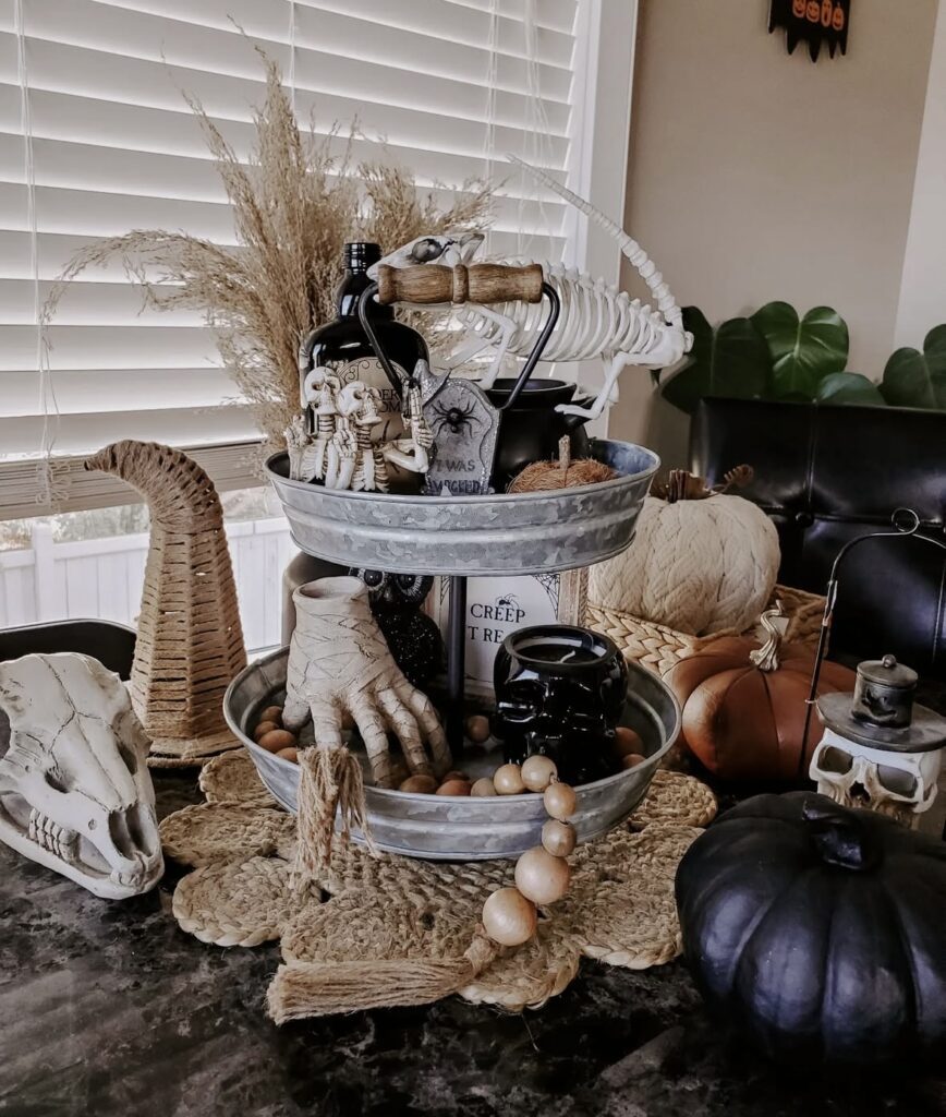Halloween tiered tray with skulls, skeleton hands, bone garlands, and mini pumpkins, perfect for a spooky-themed kitchen or coffee bar. Get ideas at www.slowestuff.com.