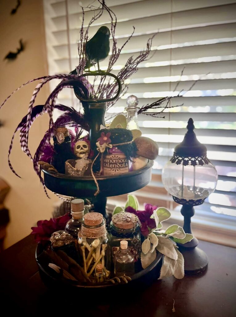 Apothecary witch tiered tray decorated with glass potion jars, black feathers, and potion labels for a New Orleans witchcore vibe. Credit: Jessika ScarletFire Roberts, www.slowestuff.com