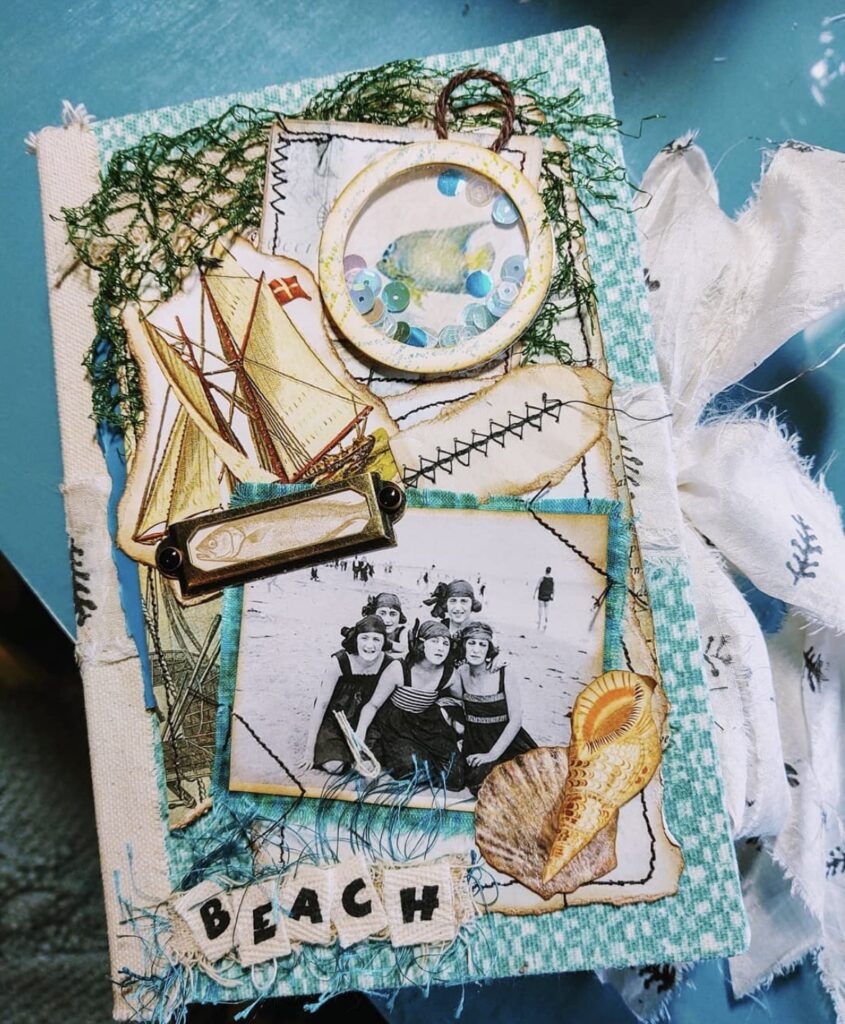 Beach junk journal cover with vintage beach girls photo, sailboat ephemera, fish shaker circle, and letter tiles spelling “BEACH.”