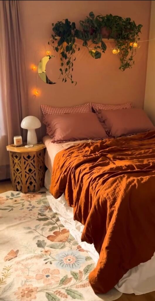 Boho fall bedroom with orange duvet, peach walls, string lights, and floral area rug for a cozy seasonal vibe.