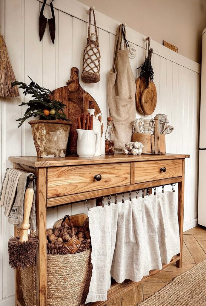 Rustic console vignette with cutting boards, linens, woven baskets, and a terracotta pot for warm autumn texture.