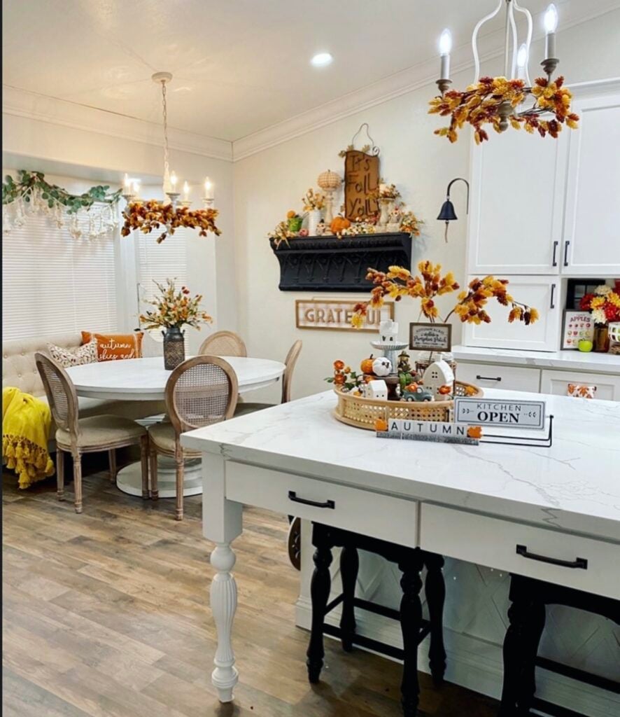 Bright breakfast nook with fall florals, playful signs, and a tiered tray centerpiece for a cheerful autumn look.