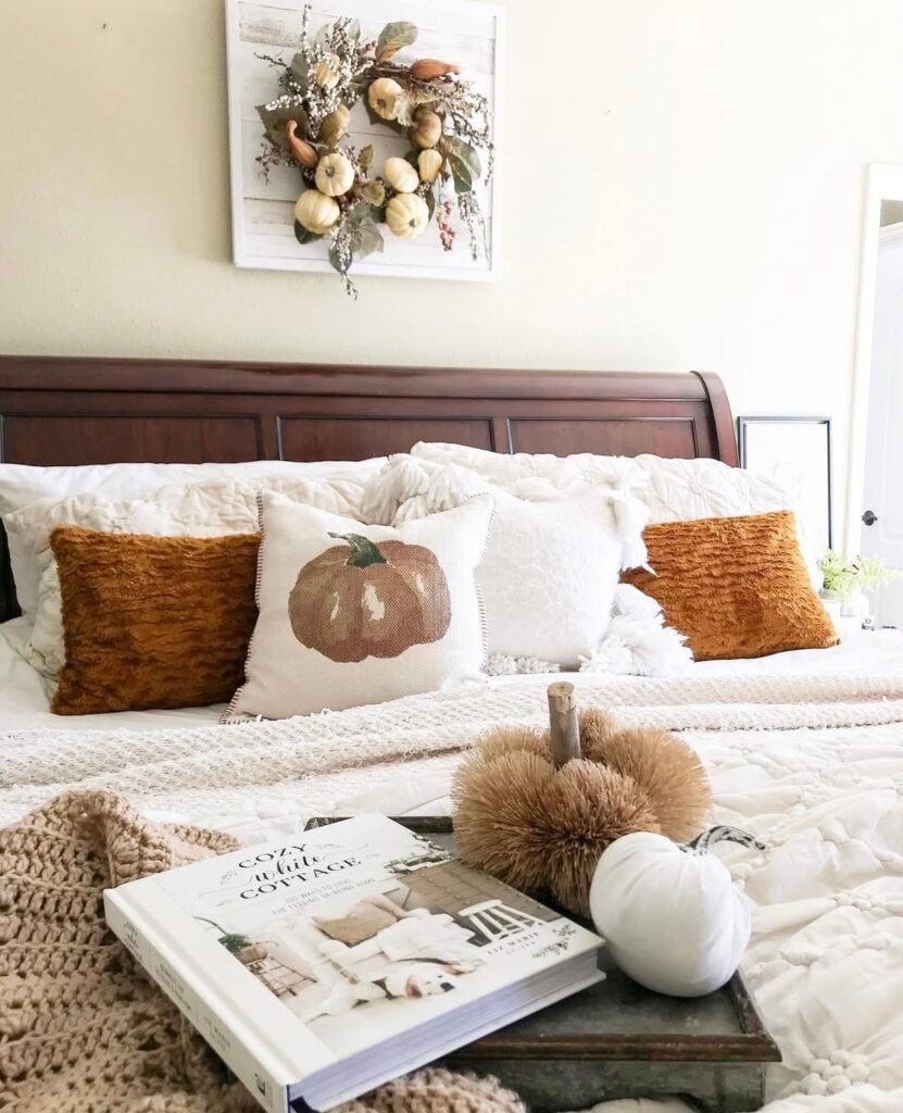 farmhouse-style fall bedroom with pumpkin throw pillow, fuzzy orange accent pillows, and a neutral chunky knit blanket