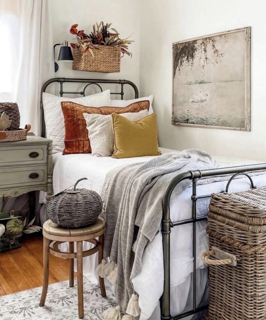 rustic fall bedroom with mustard and rust throw pillows, a black metal bed frame, and wicker pumpkin decor