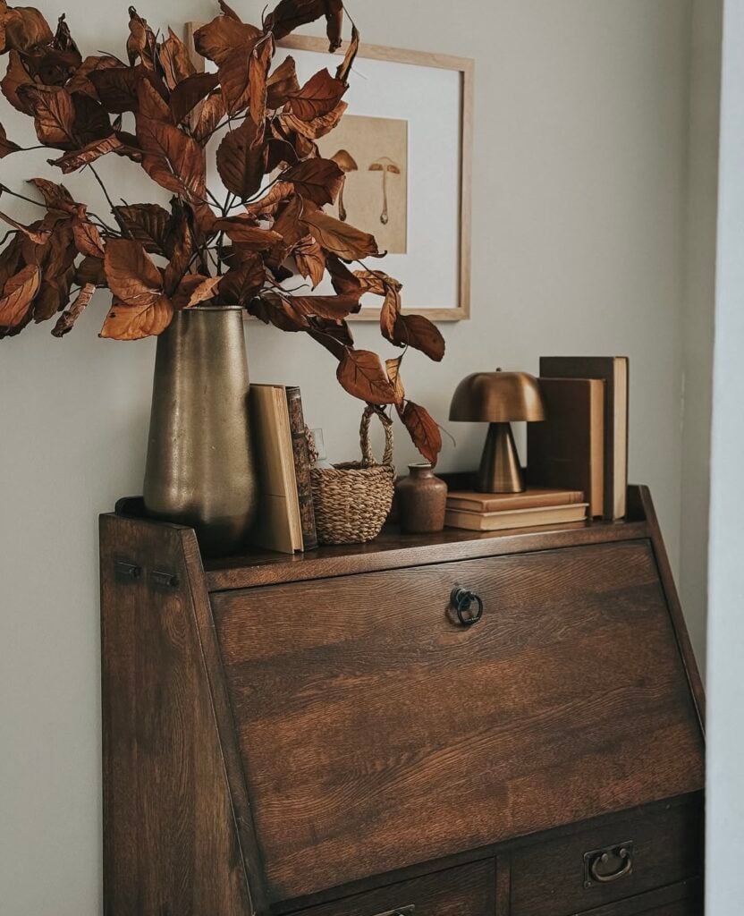 Fall entryway vignette on vintage secretary desk with dried leaves and brass accents.