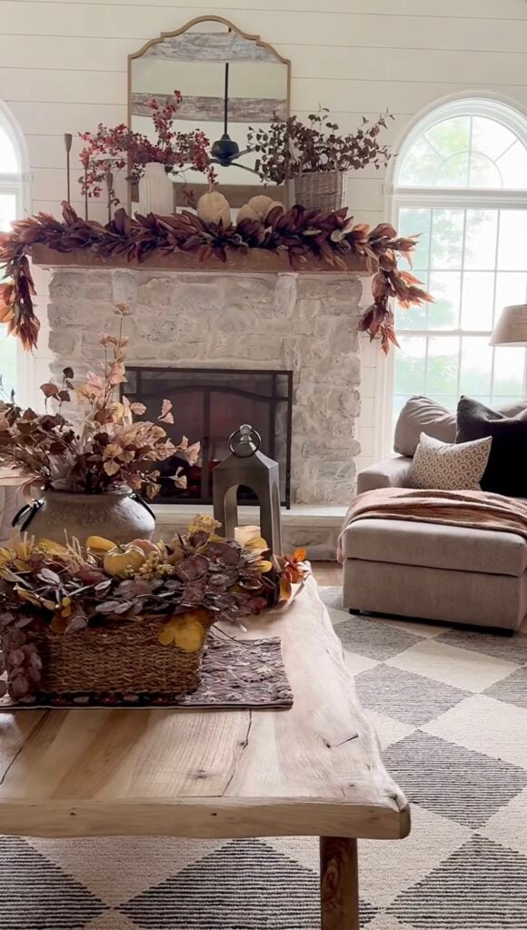 Cozy living room with stone fireplace and leafy fall mantel garland.