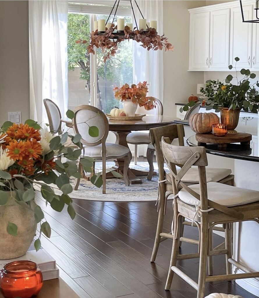 Open kitchen dining nook decorated for fall with pumpkins, orange florals, and candlelight.