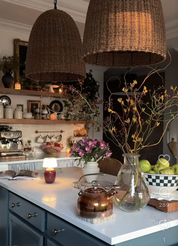 witchy kitchen island and counter with large woven lamps overhead, a glass jar filled with fall stems, a bowl of pears and other autumn accessories