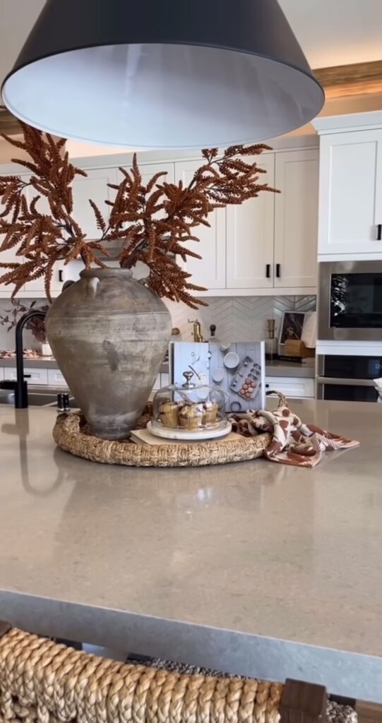 Kitchen island with large pottery urn containing fall foliage leaves with plate of muffins and seasonal dishtowel