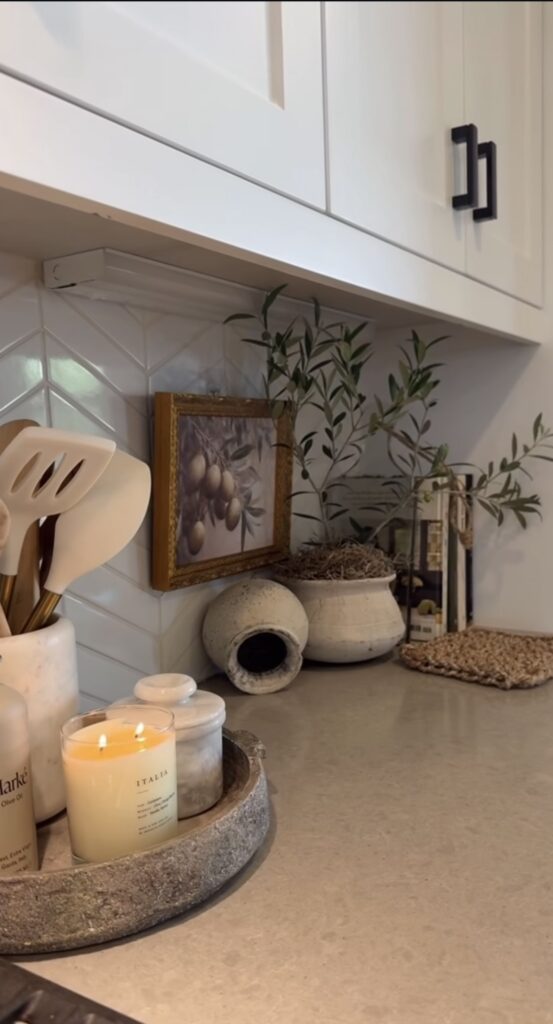 Kitchen counter with round wooden tray filled with candles plus clay pots and artwork with olive branches for subtle autumn aesthetic