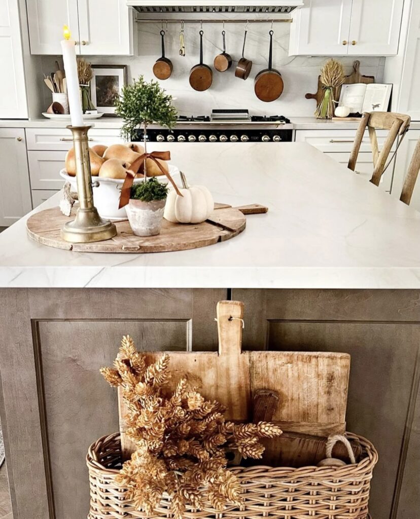 bright white kitchen showing cookware and round woven tray with candles, pears and a woven basket with fall foliage on the side of the island