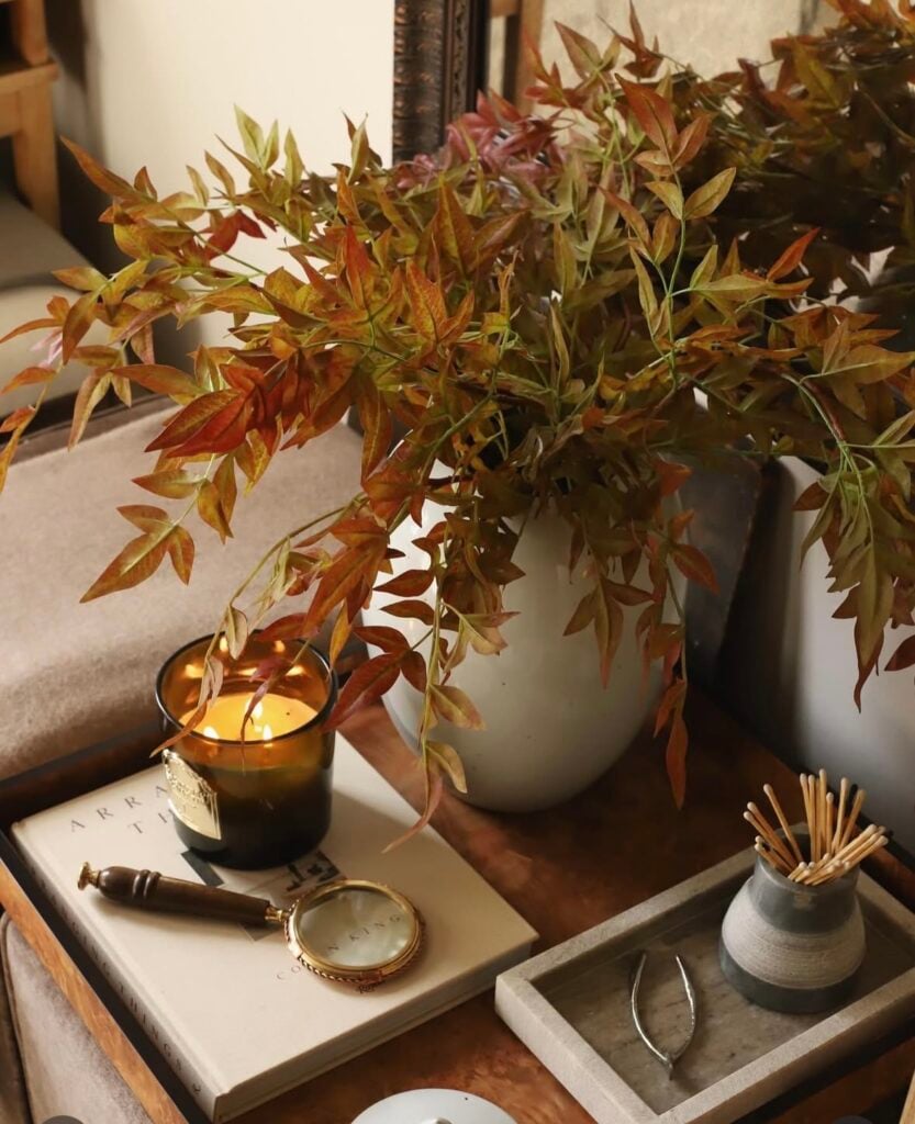 Warm side table vignette with amber candle, fall branches, and layered trays.