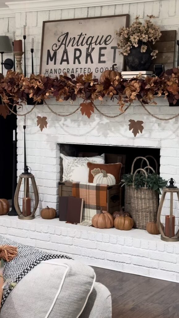 White brick fireplace styled with copper leaf garland, pumpkins, and plaid pillows.