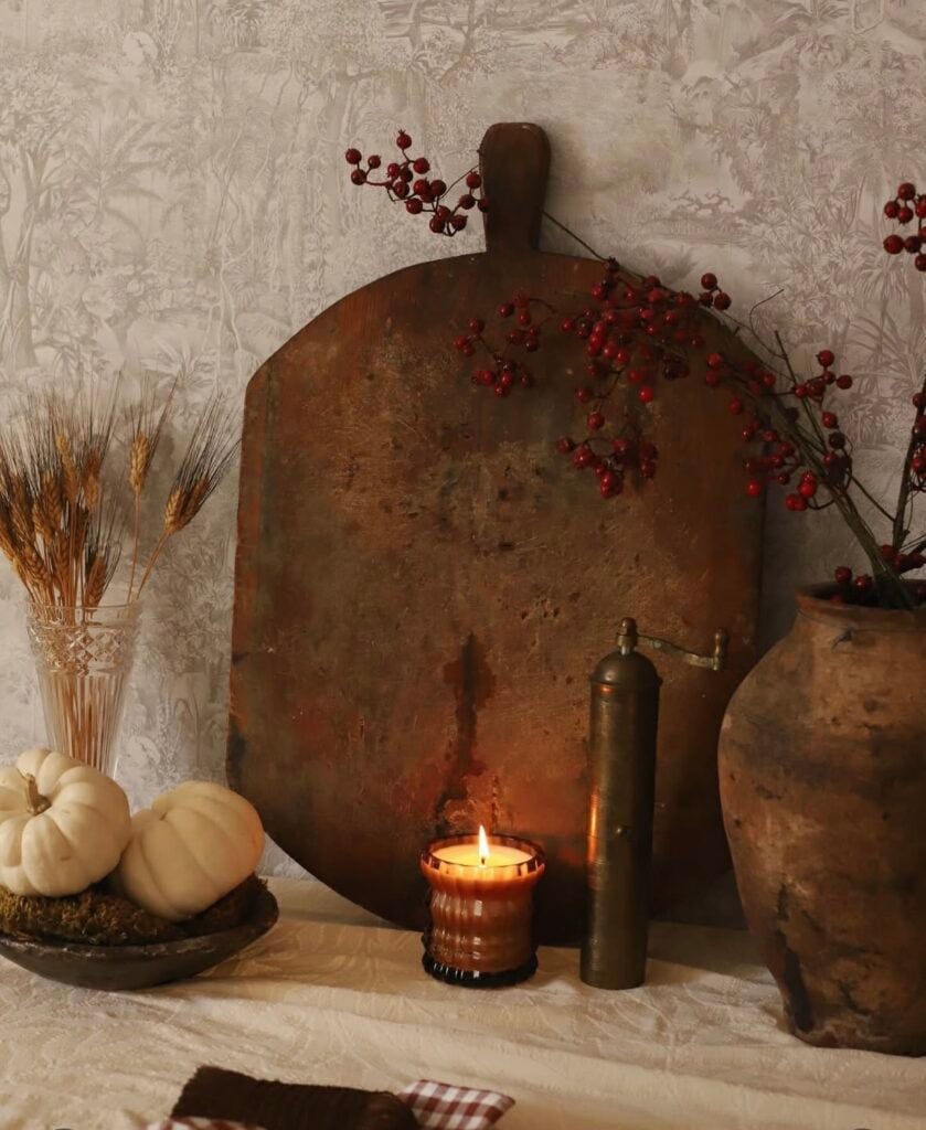 Vintage breadboard vignette with berries, white pumpkins, and a glowing candle—rustic fall style.