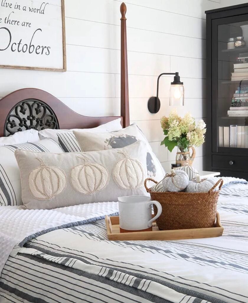 farmhouse fall bedroom with pumpkin-themed pillows, striped bedding, and a basket of fabric pumpkins on the bed