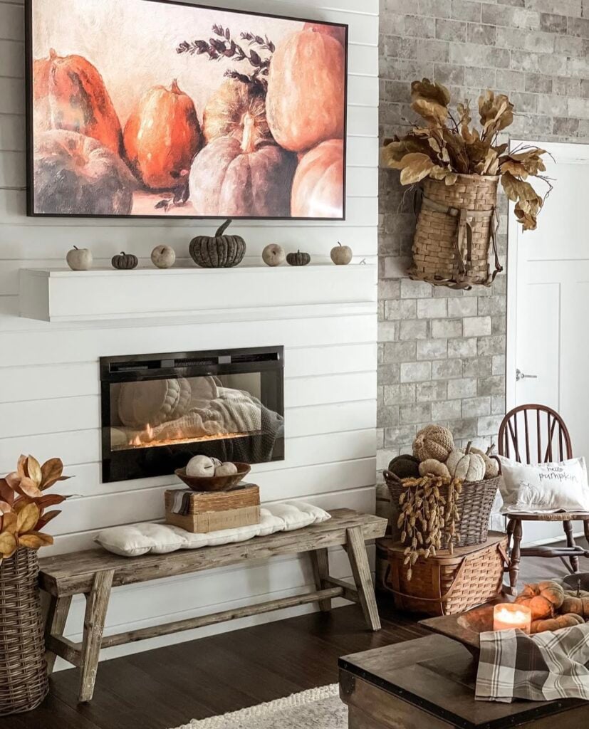 Farmhouse mantel styled for fall with pumpkin art on the frame TV and mini pumpkins along the shelf.