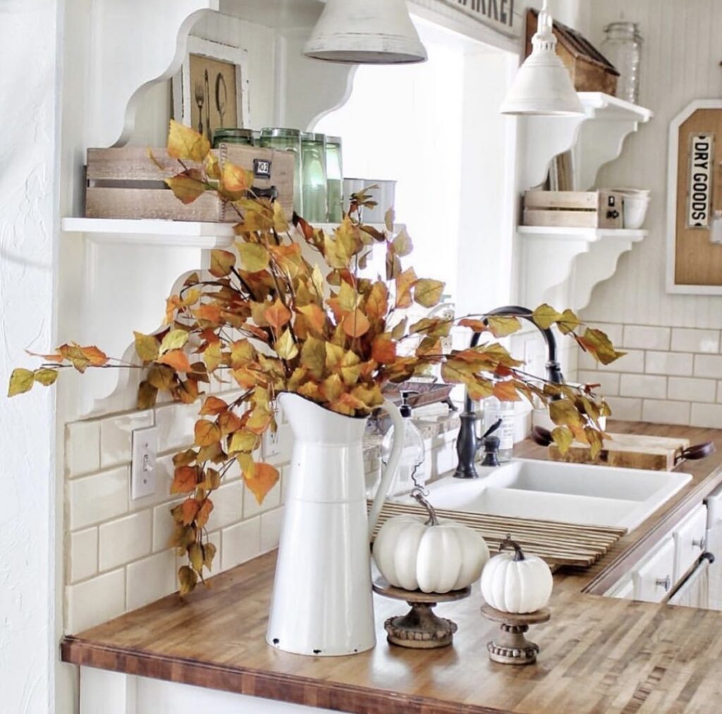 Farmhouse kitchen styled with a large fall floral arrangement, white pumpkins, and warm autumn accents on the kitchen countertop