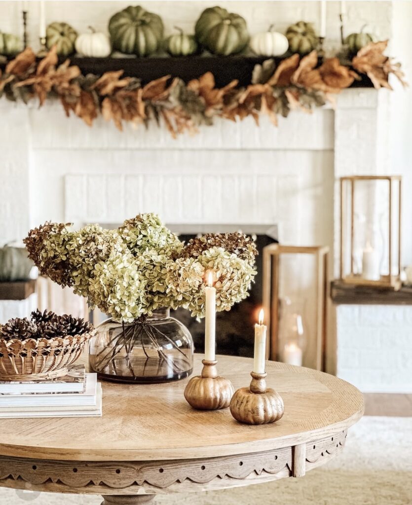 fall decor living room with white brick fireplace with leafy fall garland and pumpkins across the mantel.