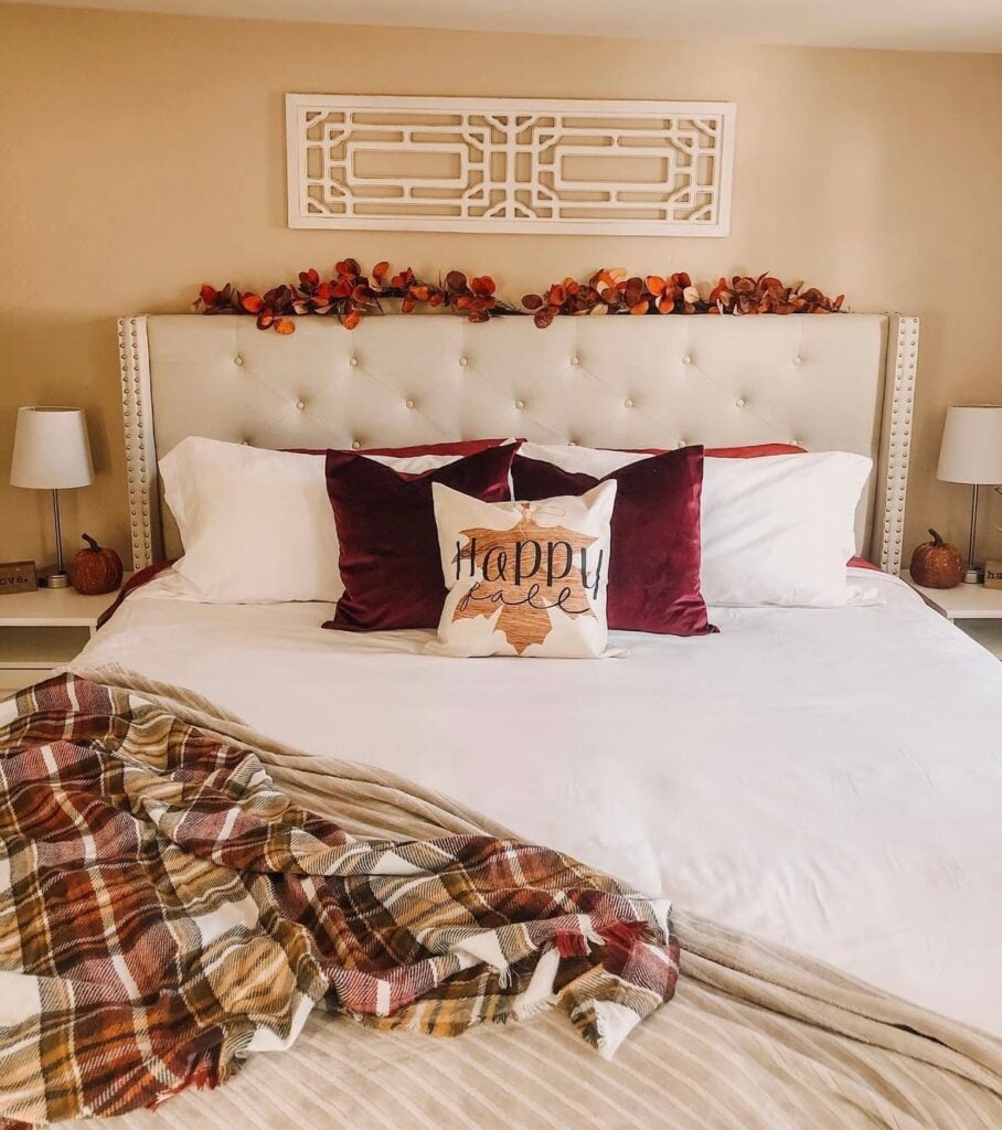 cozy fall bedroom with a “Happy Fall” throw pillow, burgundy accent pillows, and a plaid throw blanket