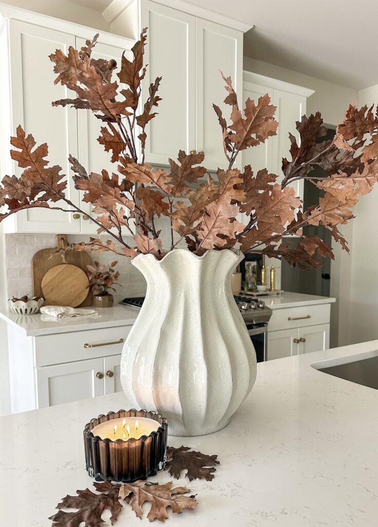 White ceramic vase filled with dried brown oak leaves on a kitchen island styled with a lit fall candle.