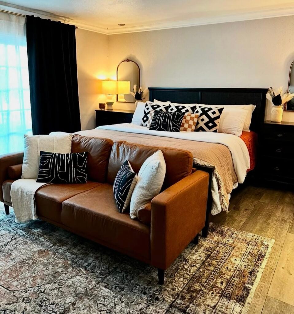 modern fall bedroom with a leather sofa at the foot of the bed, black accent pillows, and warm layered bedding