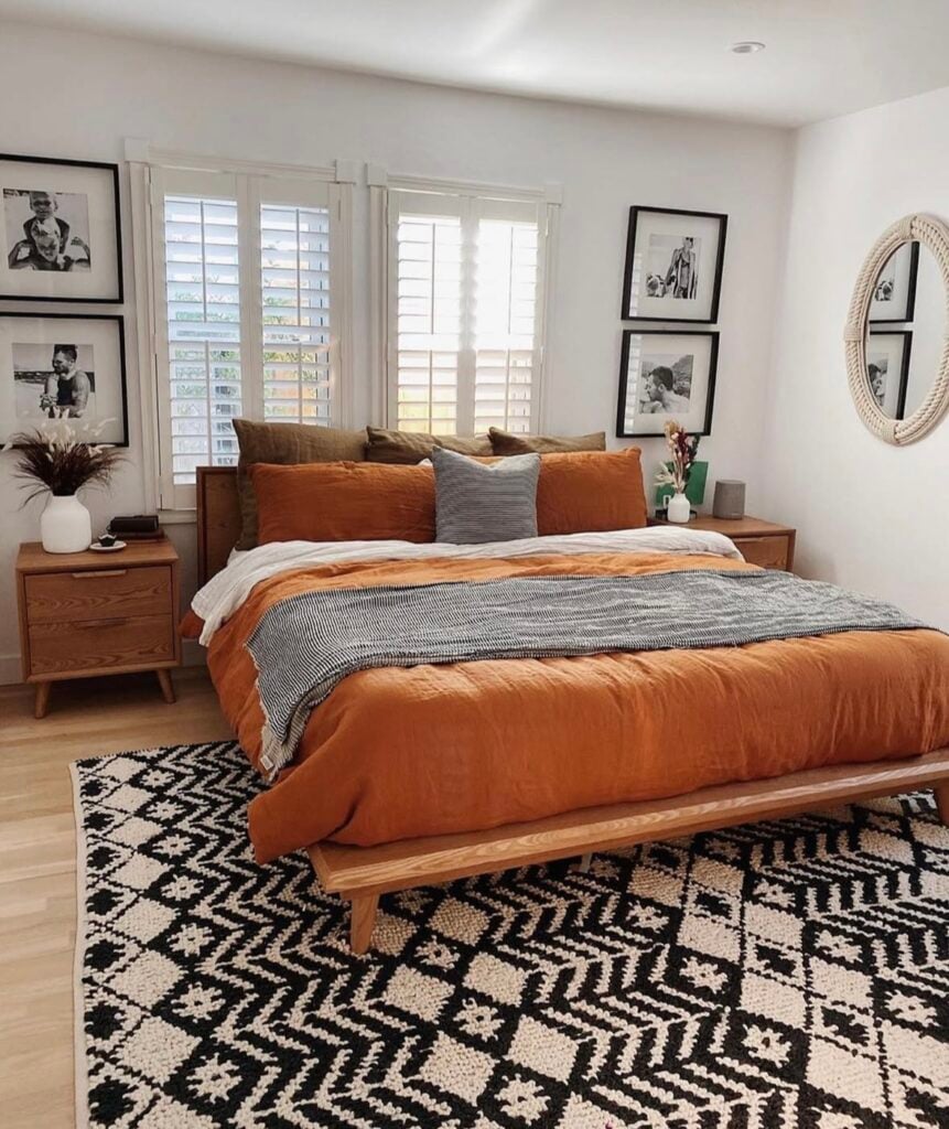 modern fall bedroom with an orange duvet, brown and gray accent pillows, and a bold black-and-white patterned rug