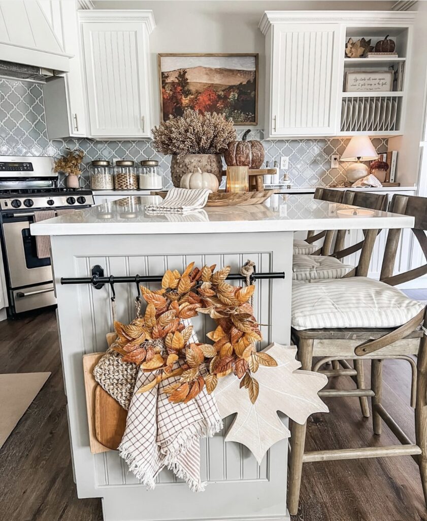 Cozy farmhouse kitchen island decorated with a golden leaf wreath, cutting boards, and neutral fall accents.