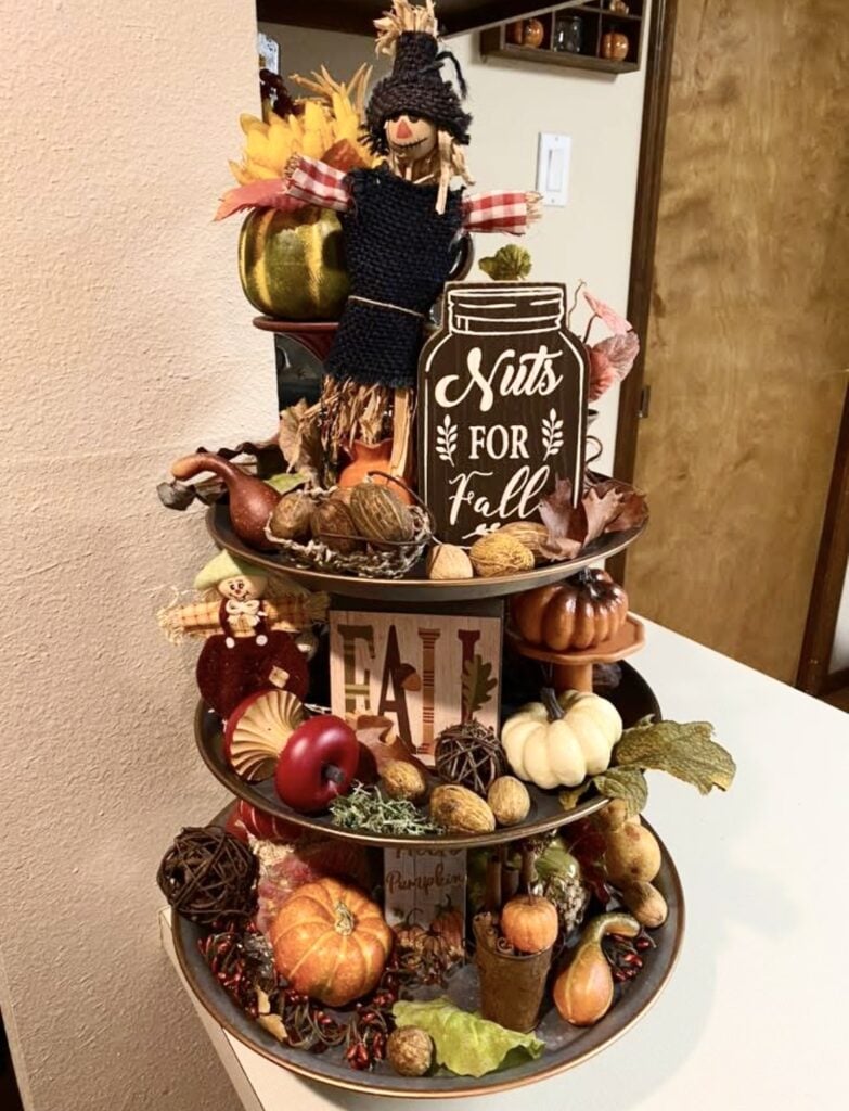 Three-tier black metal tray filled with mini ghost decorations, faux leaves, and Halloween candy in orange and white
