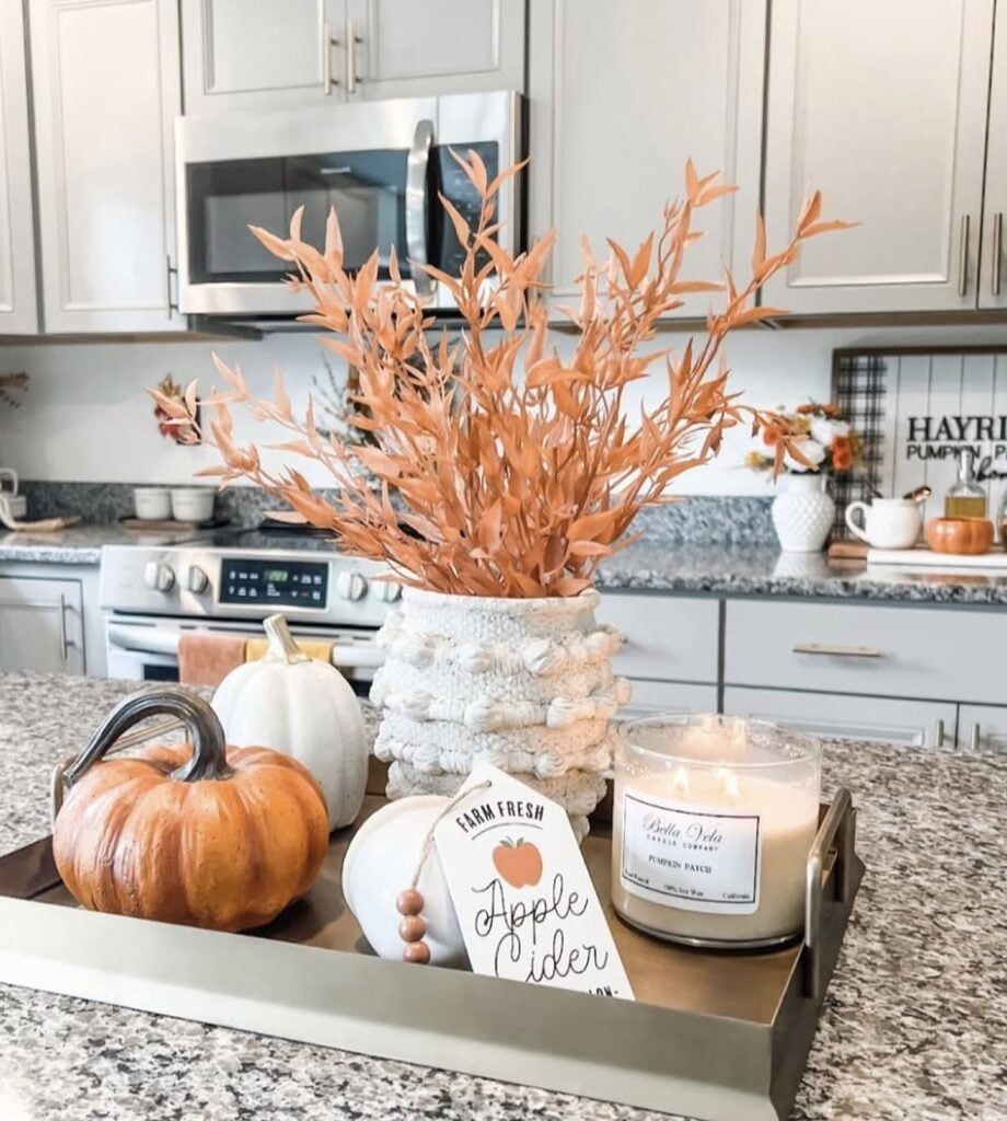Gold tray with white vase of orange leaves, pumpkins, and candle